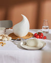 White organic-shaped burrata container by Alessi, displayed on a table with fresh garlic, tomatoes, and mozzarella.