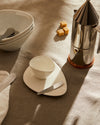 White ceramic Colombina collection tableware by Alessi, featuring organic shapes and silver cutlery, styled with brown sugar cubes and a coffee maker.