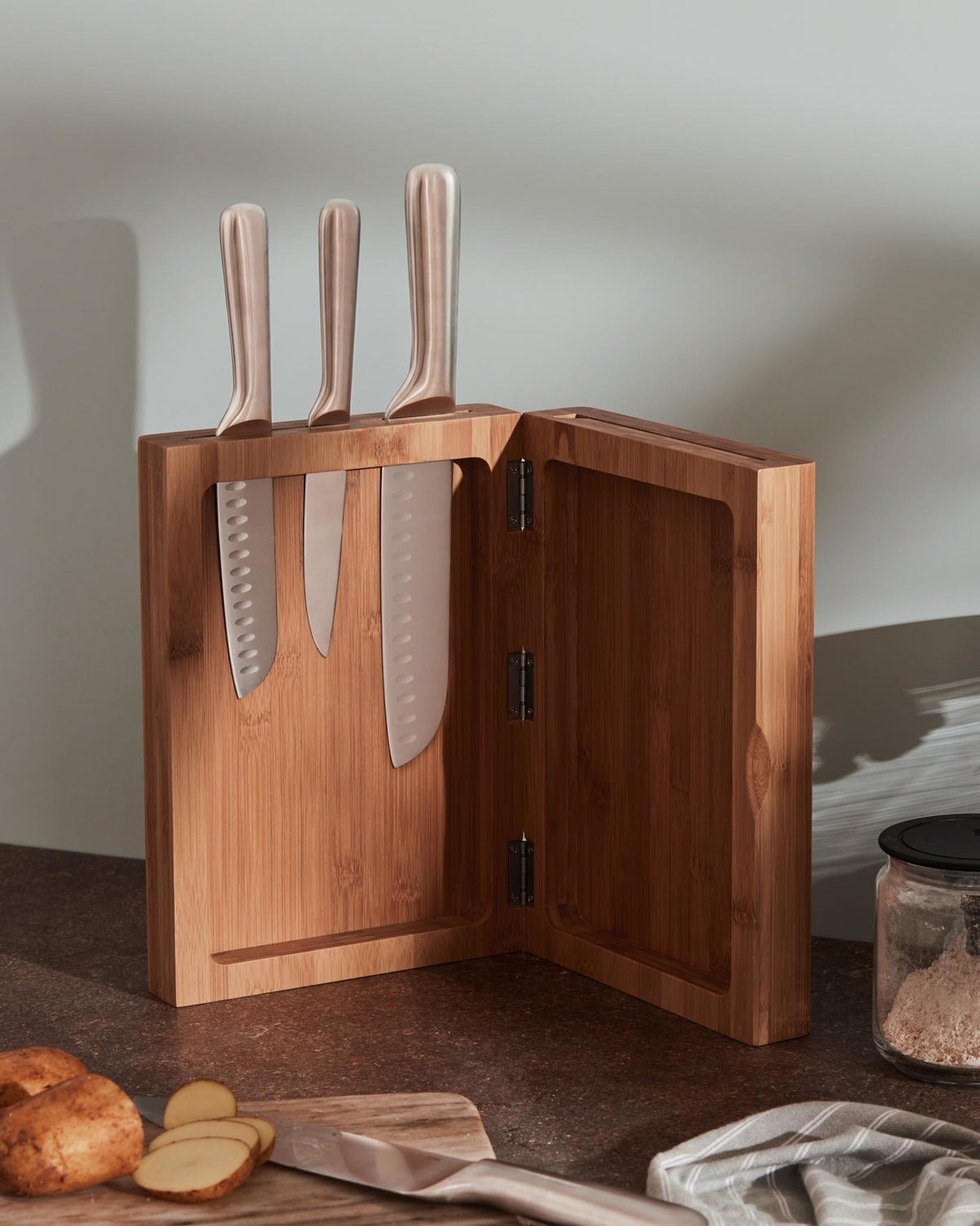 Bamboo knife block by Alessi, featuring three knives with rose gold handles, displayed open on a counter.