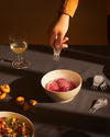 Silver metallic two-tined cocktail forks by Alessi, one held by a hand over a bowl of sliced red onions.