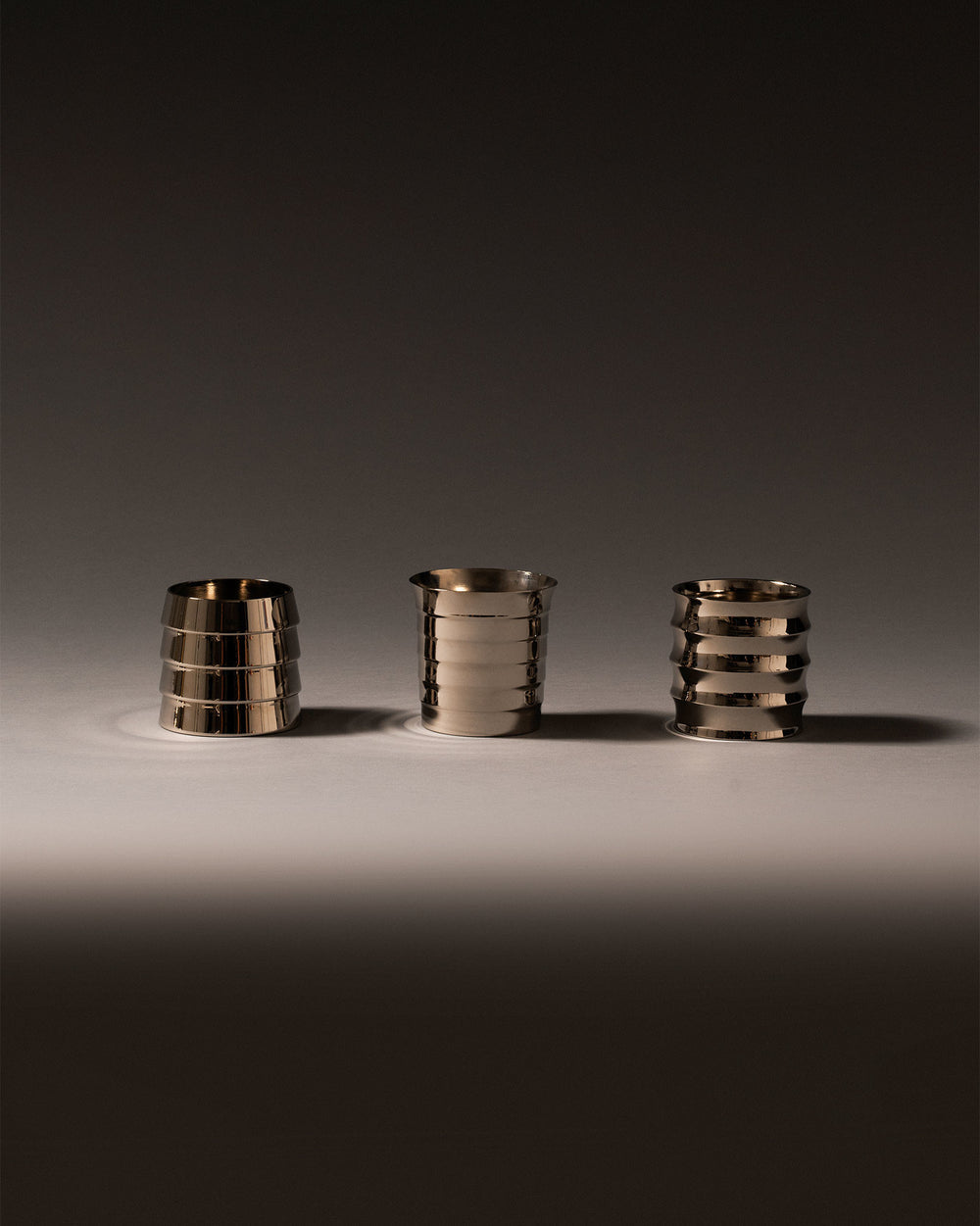 Three silver metallic Dervisci glasses by Alessi, featuring distinctive horizontal ribbed patterns on a light surface.