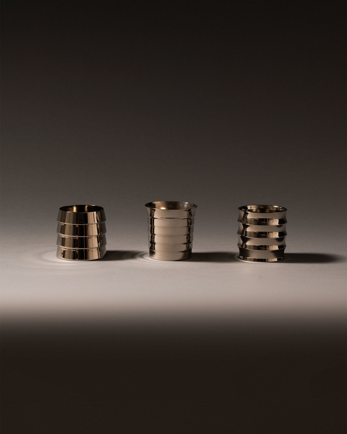 Three silver metallic Dervisci glasses by Alessi, featuring distinctive horizontal ribbed patterns on a light surface.