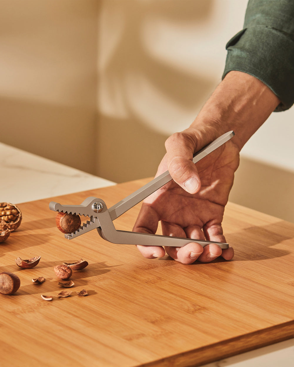 Grey metal nutcracker by Alessi, shaped like an alligator, cracking a hazelnut on a wooden board.