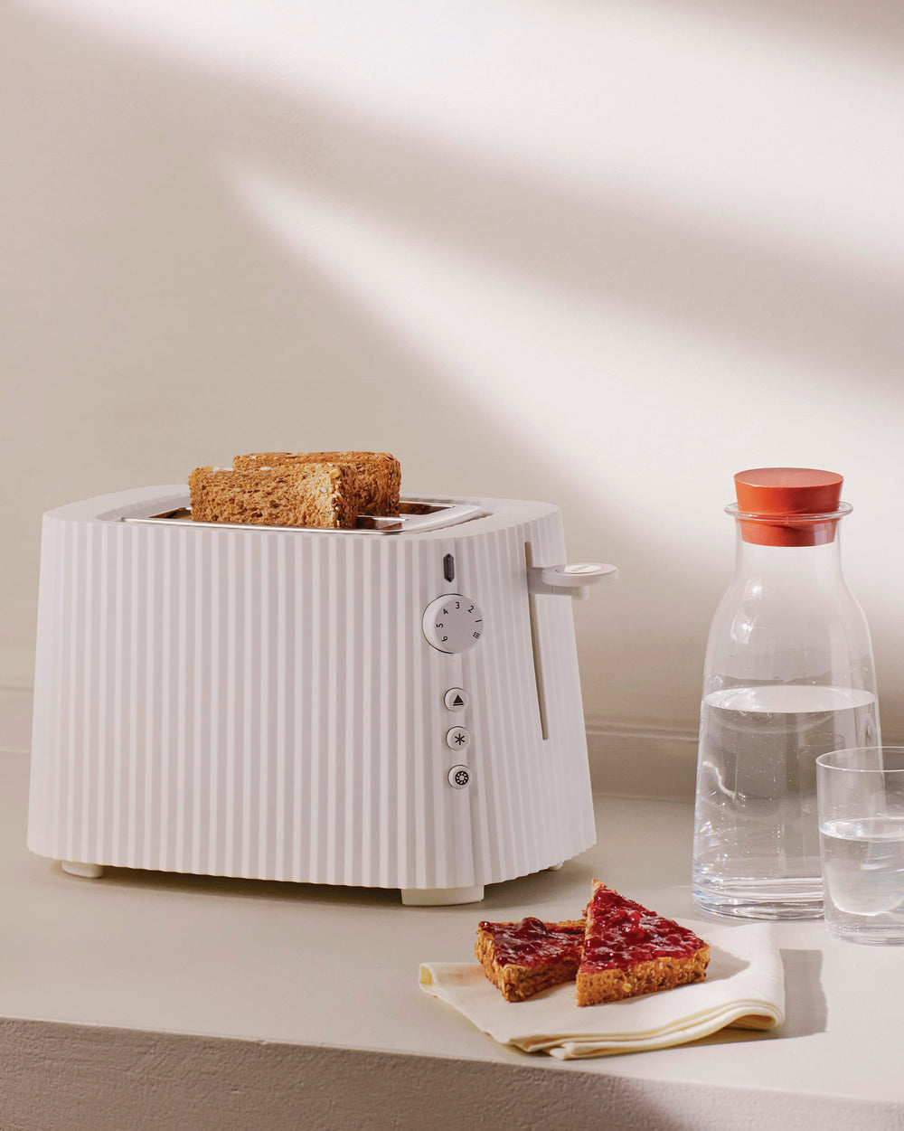 White Plissé toaster by Alessi, with vertical ridges, holding two slices of toast and jam toast.