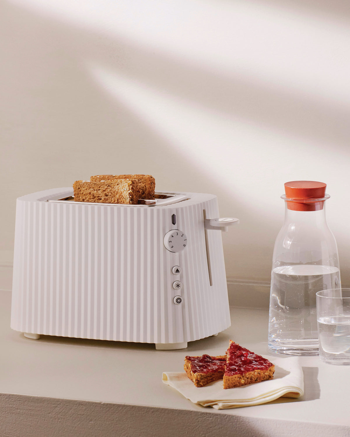 White Plissé toaster by Alessi, with vertical ridges, holding two slices of toast and jam toast.