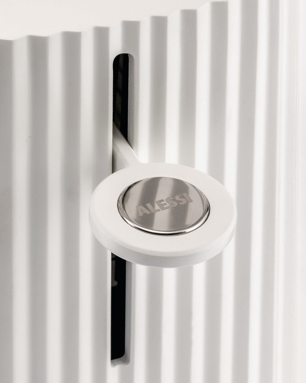 White pleated appliance by Alessi, with a round control lever and metallic logo plate.