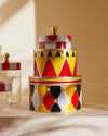 Stacked circus-themed containers by Alessi, in red, yellow, black, and white geometric patterns, with a gold finial.