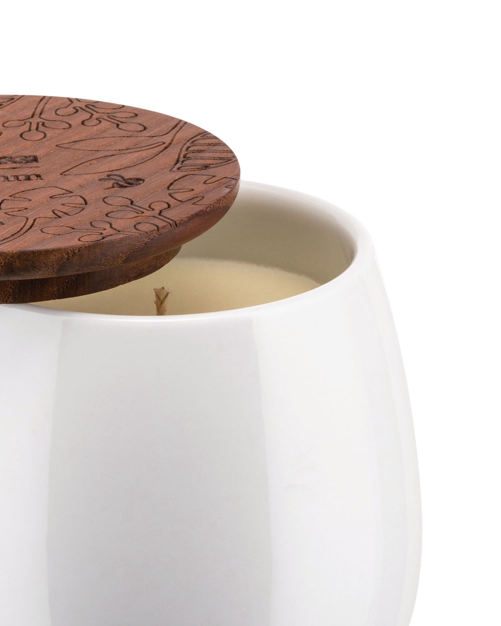 White ceramic candle by Alessi with an engraved brown wooden lid featuring a leaf pattern, partially covering the wax and wick.