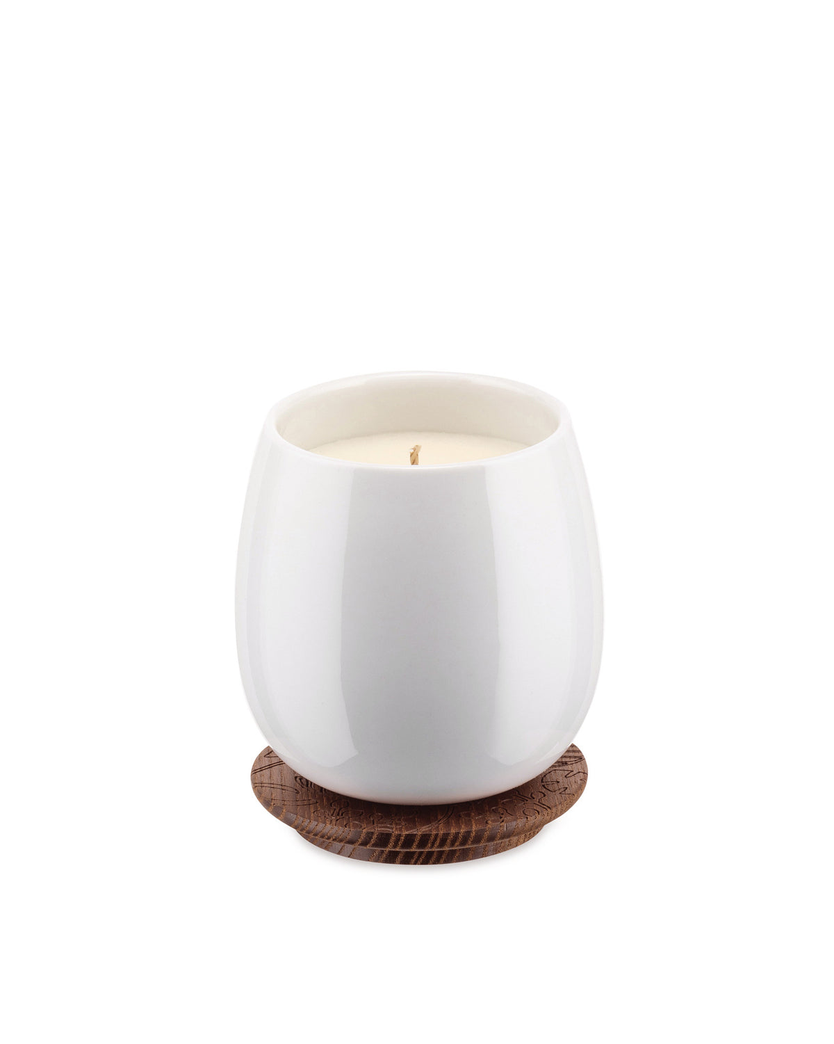 White ceramic candle by Alessi, resting on a brown wooden coaster with an engraved leaf pattern.