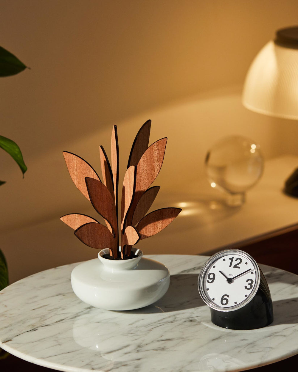 Decorative wooden plant by Alessi, with light brown abstract leaf shapes in a white vase on a marble table.