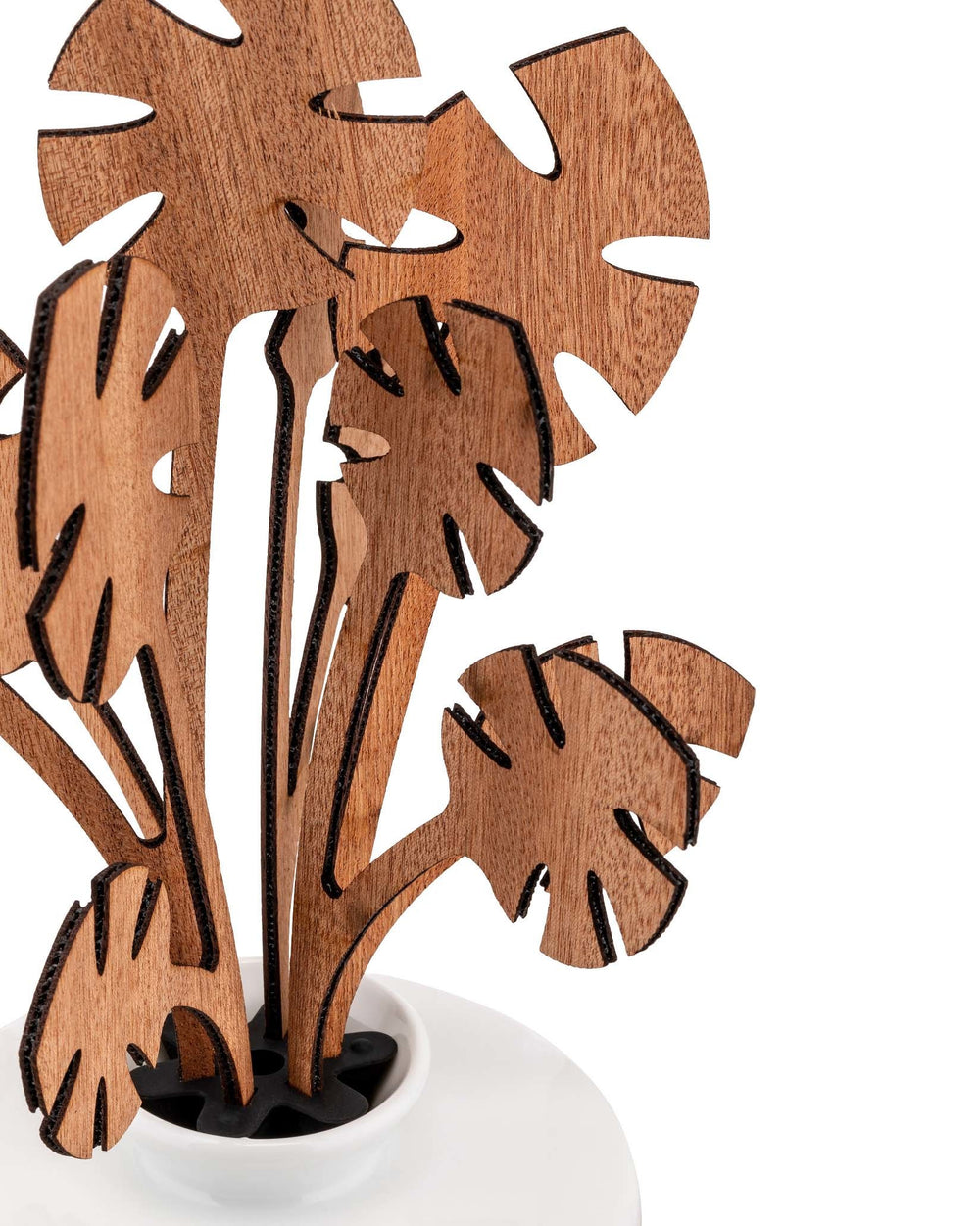 Brown wooden Monstera plant sculpture by Alessi, featuring laser-cut details and dark edges, in a white pot.