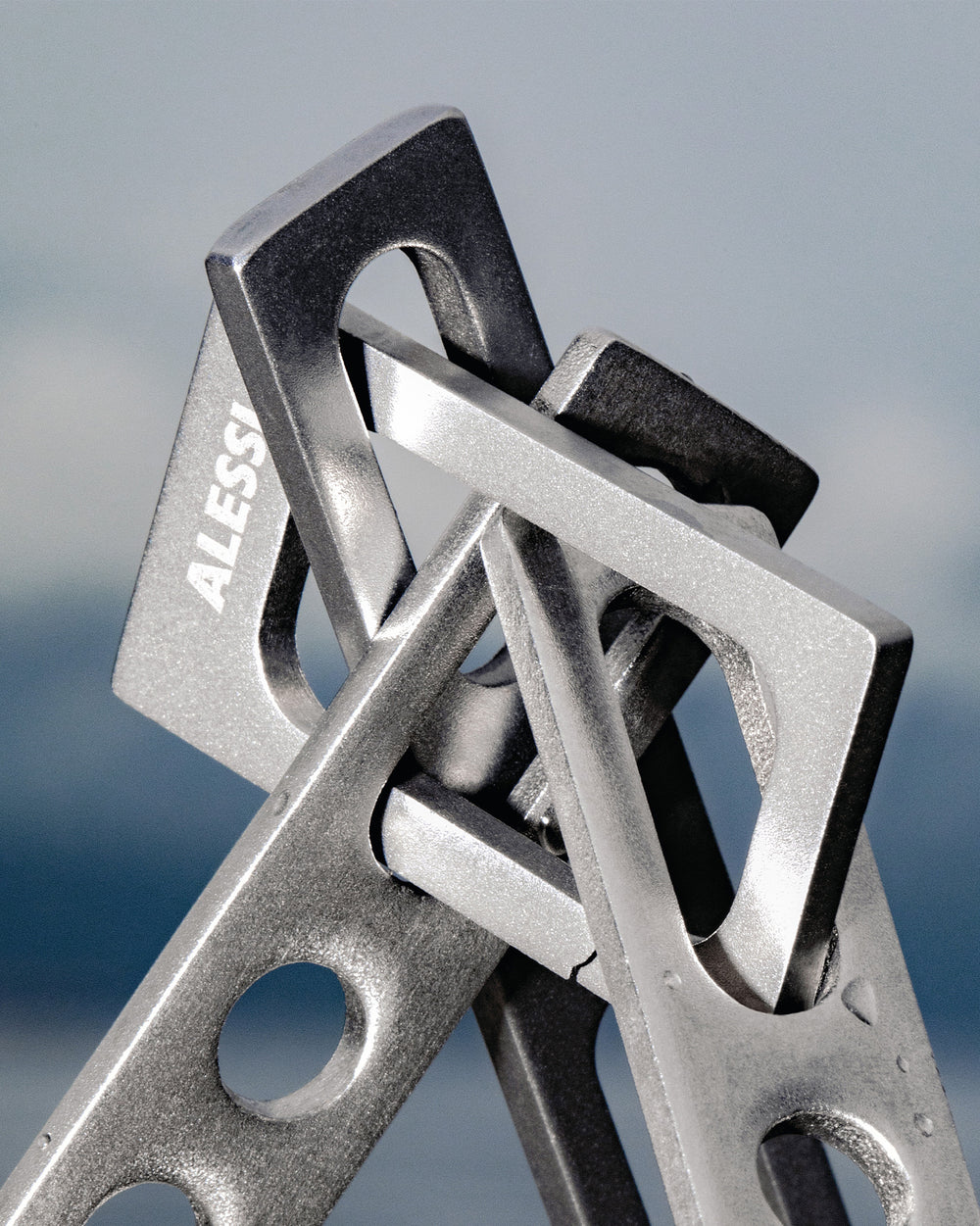 Silver-grey metal occasional object by Alessi, with 'ALESSI' etched and interlocking textured geometric shapes.