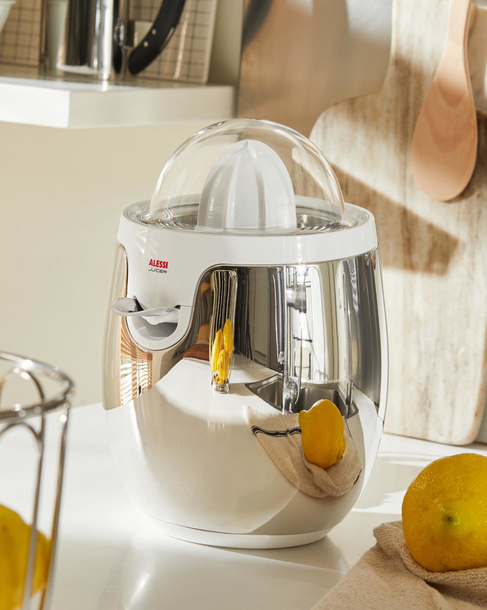 White and chrome electric juicer by Alessi, featuring a transparent dome, styled with fresh lemons on a kitchen counter.