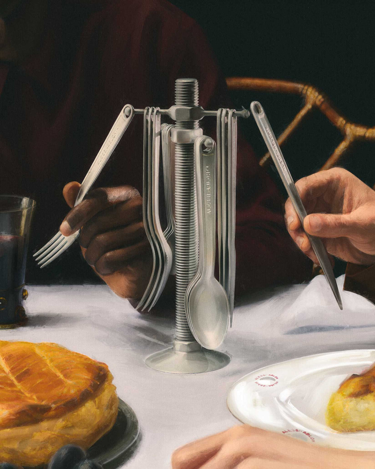 Sculptural silver cutlery holder by Alessi, with matching branded forks, spoons, and knives at a dining table.