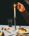 Diverse collection of conversational objects from Alessi, including a lit candle in a unique metal holder, fruit, and dessert on a table.