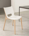 A white chair with light wood legs by Alessi, featuring a cut-out backrest, next to a dark table on a concrete floor.
