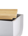 White bread bin with a light wood lid by Alessi, the bamboo lid featuring a debossed logo and partially open.